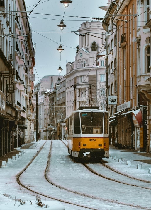 Gelbe Straßenbahn auf einer verschneiten Straße mit alten Stadthäusern