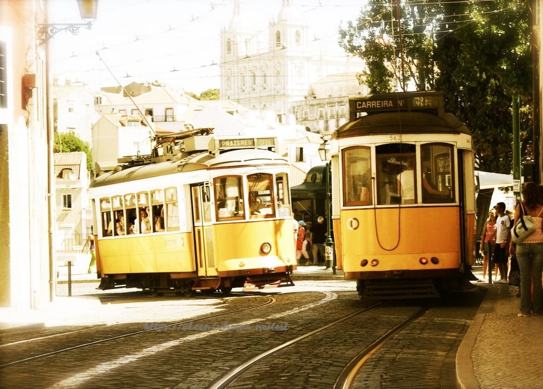 Zwei gelbe Straßenbahnen kreuzen sich auf einer Straße in Lissabon vor einer Kirchenkuppel