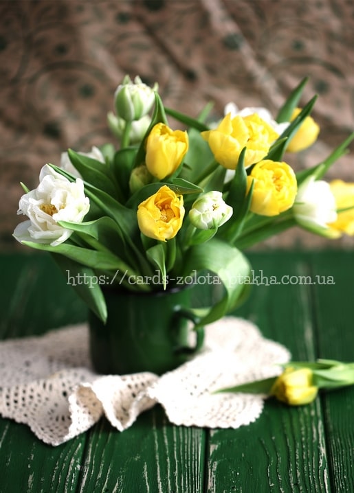 Strauß aus gelben und weißen Tulpen in einem dunkelgrünen Emaille-Becher auf Holztisch